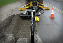 Excavator with a Digga Bigfoot Trencher digging a trench.